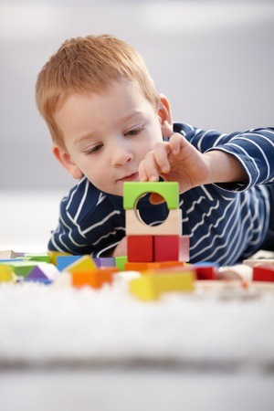 Sweet gingerish little boy building tower from cubes at home, laying on floor. @nyul